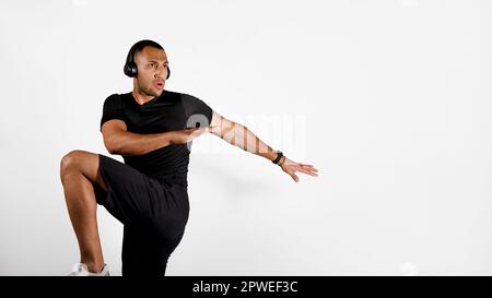Afrikanischer Mann, Der Ellbogen-Knie-Training Mit Kopfhörern Macht, Studio Stockfoto