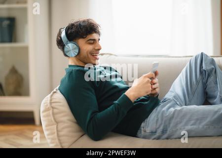 Seitenansicht Des Mannes Mit Smartphone Mit Kopfhörern Zu Hause Stockfoto