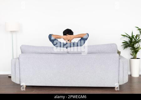 Entspannter Kerl, der zu Hause auf der Couch chillt, Rückansicht Stockfoto
