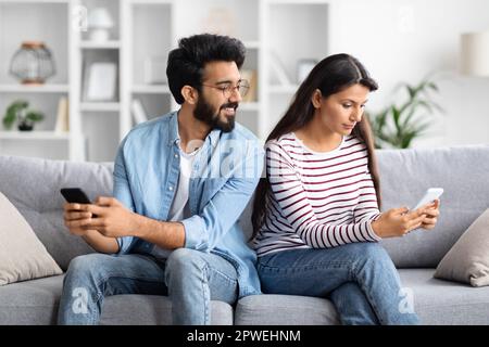 Junge indische Frau, die Handy benutzt, Ehemann, der spioniert Stockfoto