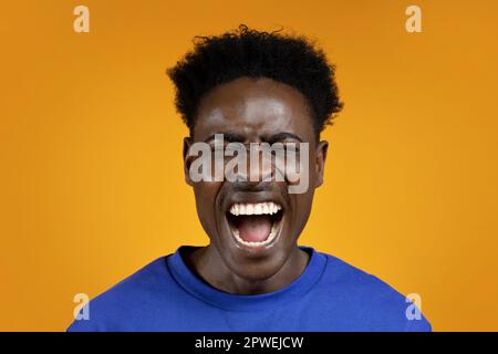 Foto eines emotional schreienden jungen afrikaners auf Gelb Stockfoto