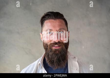 Portrait eines glücklichen Hipsters aus nordeuropa - selbstbewusster und lächelnder bärtiger Mann mit eigenartigen blauen Augen, der Spaß hat, während er vor den Reisenden posiert Stockfoto