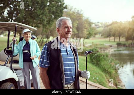 Ich genieße ein sonniges Spiel. Ein lächelndes Seniorenpaar genießt einen Tag auf dem Golfplatz. Stockfoto