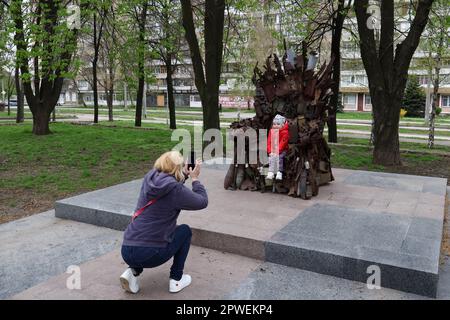 Zaporischschien, Ukraine. 15. April 2023. Die Frau eines ukrainischen Soldaten wird dabei gesehen, wie sie ein Foto von ihrer Tochter am Eisernen Thron des Ostens im Zentrum von Zaporischschien macht. Der Eiserne Thron des Ostens in Zaporischzhien, Ukraine, der aus echten militärischen Maschinen, Trümmern und Granaten besteht. Er wurde im Winter 2016 an den Positionen der Streitkräfte der Ukraine in der Stadt Avdiivka in der Region Donezk hergestellt. Der Eiserne Thron des Ostens wurde in der Stadt Zaporischhien mit Unterstützung von örtlichen Hilfssheriffs errichtet - Kriegsveteranen. Er würdigt den herausragenden Willen des ukrainischen Volkes, zu gewinnen. Autoren Stockfoto