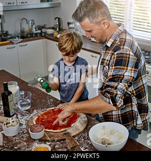 Pizzas, unsere Lieblingsmahlzeit. Ein Vater und sein Sohn machen Pizza zu Hause. Stockfoto