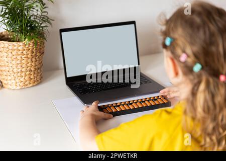 Ein Mädchen von hinten ist in der mentalen Arithmetik auf dem Abakus aktiv, online auf einem Laptop, Chroma Key Hintergrund. Das Konzept, Kindern das beizubringen Stockfoto