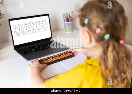 Ein Mädchen von hinten ist in der mentalen Arithmetik auf dem Abakus aktiv, online auf einem Laptop, Chroma Key Hintergrund. Das Konzept, Kindern das beizubringen Stockfoto