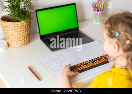 Ein Mädchen von hinten ist in der mentalen Arithmetik auf dem Abakus aktiv, online auf einem Laptop, Chroma Key Hintergrund. Das Konzept des Lehrens von Kindern zum Lernen Stockfoto