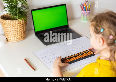 Ein Mädchen von hinten ist in der mentalen Arithmetik auf dem Abakus aktiv, online auf einem Laptop, Chroma Key Hintergrund. Das Konzept, Kindern das beizubringen Stockfoto