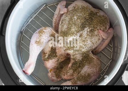 Rohes Hähnchen mit gemischten Kräutern auf einem Regal in einer Airfryer, das sich auf das Kochen vorbereitet. Gesundes, kostengünstiges Kochkonzept Stockfoto