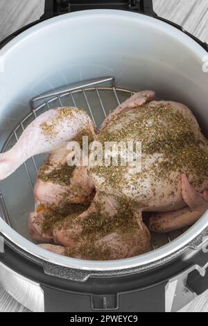 Rohes Hähnchen mit gemischten Kräutern auf einem Regal in einer Airfryer, das sich auf das Kochen vorbereitet. Gesundes, kostengünstiges Kochkonzept Stockfoto