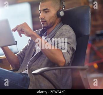 Musik macht alles besser. Ein Designer, der Musik auf einem digitalen Tablet im Büro hört. Stockfoto