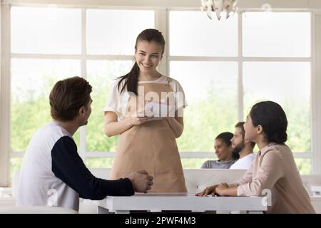 Die junge Kellnerin in der Schürze nimmt die Bestellung von einem Paar entgegen Stockfoto