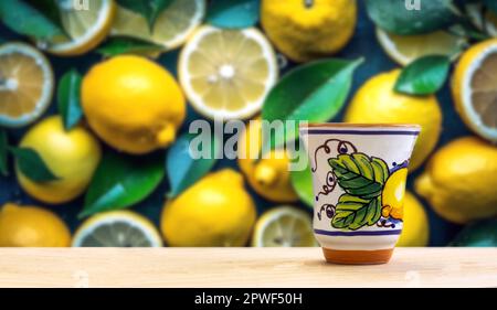 Traditioneller hausgemachter Zitronenlikör Limoncello und frische Zitrusfrüchte, selektiver Fokus auf ein Zitronenfeld im Hintergrund an einem sonnigen Tag. Vorderansicht. Horizontal Stockfoto