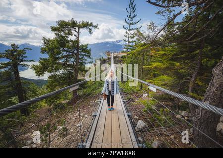 Ein blonder, weiblicher Tourist genießt die kanadische Wildnis auf einer Hängebrücke von der Sea to Sky Gondola in der Nähe von Squamish, B.C., Kanada. Stockfoto