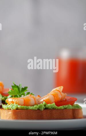 Gesunder Snack oder Garnelen-Bruschetta mit Avocado und Brot. Gebratene Garnelen und zerdrückte Avocado auf getoastetem Brot Stockfoto