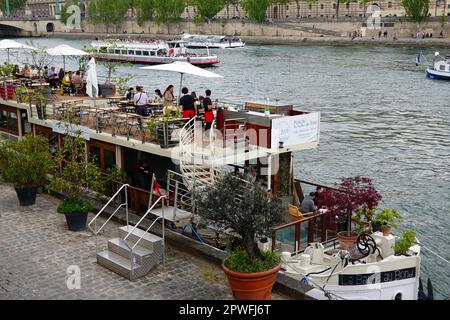 Menschen essen Mittagessen auf der umgebauten peniche La Balle au Bond, während Boote an der seine vorbeifahren, Paris, Frankreich. Stockfoto