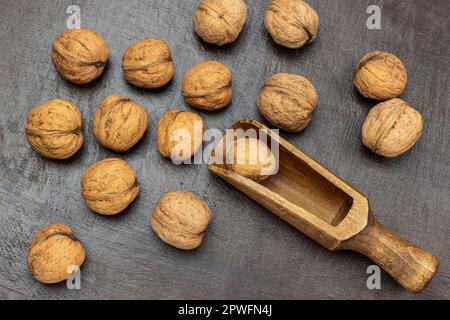 Ganze Nüsse und eine Holzschaufel auf braunem Hintergrund. Flach verlegt Stockfoto