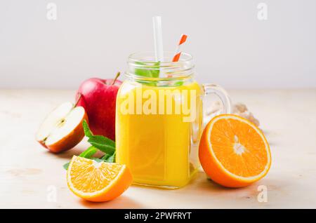 Frischer Smoothie mit Orange, Apfel und Ingwer in einem Glasgefäß, Vitamingetränk, Detox, erfrischender Cocktail auf hellem Hintergrund Stockfoto