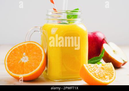 Frischer Smoothie mit Orange, Apfel und Ingwer in einem Glasgefäß, Vitamingetränk, Detox, erfrischender Cocktail auf hellem Hintergrund Stockfoto