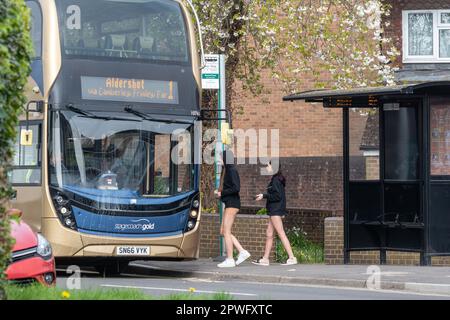 Zwei Mädchen im Teenageralter in Shorts, die an einer Bushaltestelle in Surrey, England, in einen Bus einsteigen. Öffentliche Verkehrsmittel, Alltag, 2023 Stockfoto