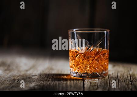 Whiskey mit Eis oder Brandy in einem Glas auf einem rustikalen Holztisch. Whiskey mit Eis in einem Glas. Whiskey oder Cognac in einem Glas. Selektiver Fokus. Stockfoto