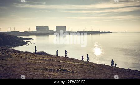 Eine Gruppe junger Leute in einer Silhouette gegen das Kernkraftwerk in Heysham, Lancashire, Großbritannien Stockfoto