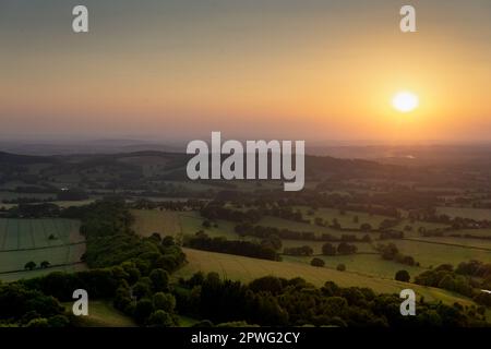 Eine Gruppe von Menschen, die die Schönheit der Natur bei Sonnenaufgang bewundern und beobachten, wie die Sonne über einem entfernten Horizont über einen malerischen Hügel aufgeht. Malver Hills Stockfoto