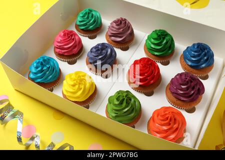 Schachtel mit verschiedenen Cupcakes und Konfetti auf gelbem Hintergrund, Nahaufnahme Stockfoto