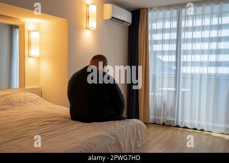 Adipositas Mann saß leider im Bett im Urlaub allein im Hotel, ohne Freunde, die eine Midlife Crisis hatten. Stockfoto