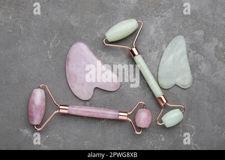 Verschiedene Gua-sha-Steine und Gesichtsrollen auf grauem Tisch, flach liegend Stockfoto