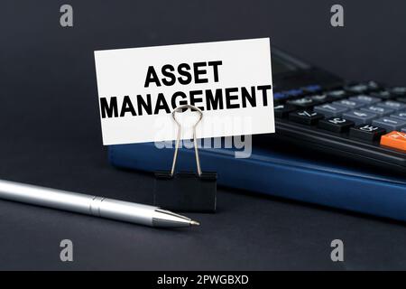 Geschäftskonzept. Auf dem Tisch befinden sich ein Notizbuch, ein Taschenrechner, ein Stift und eine Visitenkarte mit der Aufschrift „Asset Management“ Stockfoto