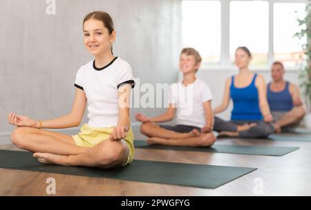 Teenager-Mädchen mit ihren Eltern praktiziert Yoga in Lotusposition Stockfoto