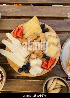 Verschiedene leckere Käsescheiben, zubereitet mit Erdbeeren und Obst auf einem Holztisch Stockfoto