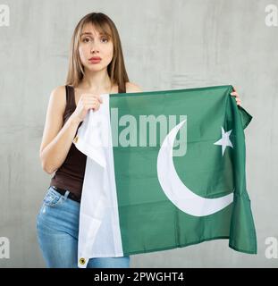 Traurige junge Frau, die vor eingefärbtem Hintergrund die Flagge Pakistans hält Stockfoto