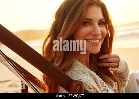 Ich finde es tröstlich, am Strand zu sein. Porträt einer jungen Frau, die sich auf einer Liege am Strand entspannt. Stockfoto