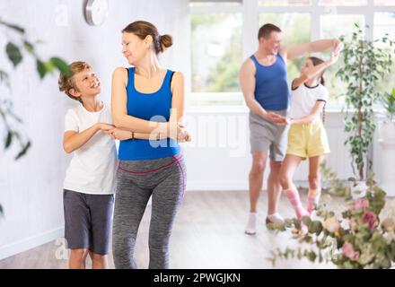 Glückliche Mutter und Sohn, die zusammen mit anderen Familienmitgliedern Tanzen üben Stockfoto