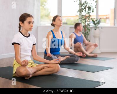 Teenager-Mädchen mit ihren Eltern praktiziert Yoga in Lotusposition Stockfoto