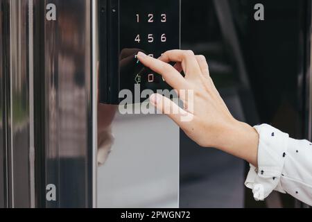 Die Hand einer Frau, die eine Sprechanlage am Eingang des Gebäudes benutzt. Mit einem elektronischen Schloss Stockfoto