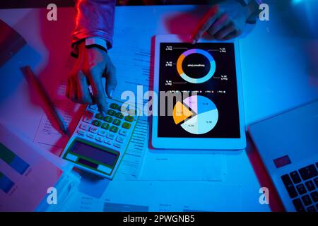 Obersicht der modernen Frau mit Taschenrechner und Dokumenten, die Diagramme untersuchen und Tablet-PCs in modernen Büros einsetzen. Stockfoto