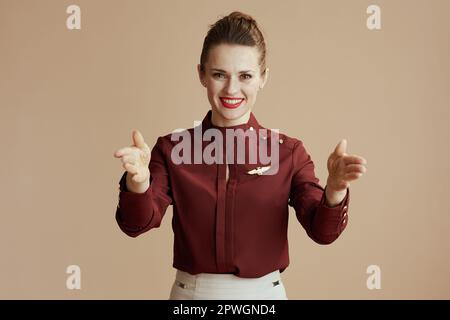 Lächelnde, stilvolle Stewardess isoliert auf beigem Hintergrund, die zeigt, wo die Ausgänge sind. Stockfoto