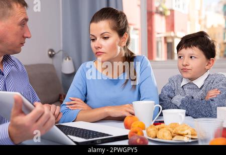 Ein Mann mit Laptop, der seiner besorgten Frau und seinem Sohn alles erklärt Stockfoto