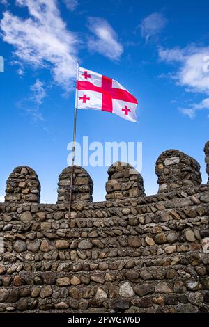 Die Flagge Georgiens, die auf hellblauem Hintergrund winkt, und die alten sighnaghi-Mauern. Stockfoto