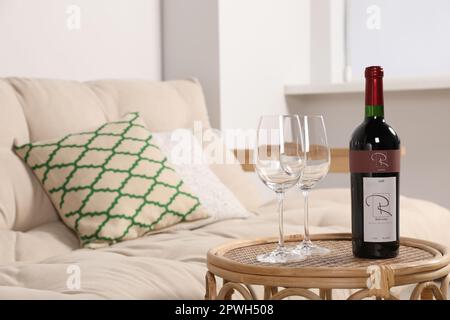 Gläser und Wein auf einem Rattantisch neben dem Sofa im Wohnzimmer. Innendesign Stockfoto