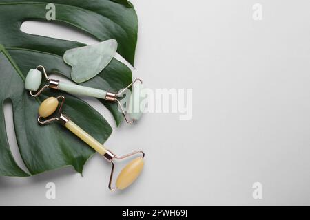 Gua-sha-Stein, verschiedene Gesichtsrollen und Monstera-Blatt auf hellem Hintergrund, flach liegend. Platz für Text Stockfoto