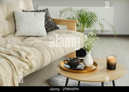 Sofa und runder Holztisch mit dekorativen Elementen im Wohnzimmer. Innendesign Stockfoto