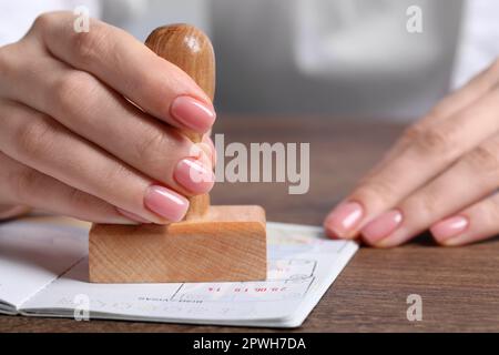 Ukraine, Lemberg - 6. September 2022: Frau stempelt Visumseite im Reisepass am Holztisch ab, Nahaufnahme Stockfoto