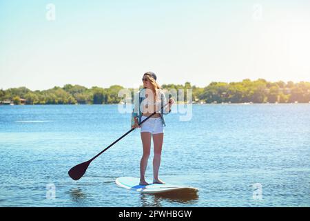 Allein zu sein war noch nie eine ruhigere Erfahrung. Eine attraktive junge Frau, die auf einem See paddelt. Stockfoto