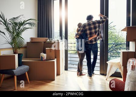 Das ist unser Neuanfang. Rückansicht eines entspannten Paares mittleren Alters, das sich gegenseitig festhält, während es auf den Balkon in seinem neuen Zuhause schaut. Stockfoto