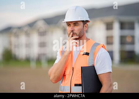 Baumeister-Denken. Bauarbeiter im Helm bauen ein neues Haus. Ingenieure arbeiten in Baukleidung und Schutzhelm. Foreman Porträt im Freien. 40s Arbeiter Stockfoto